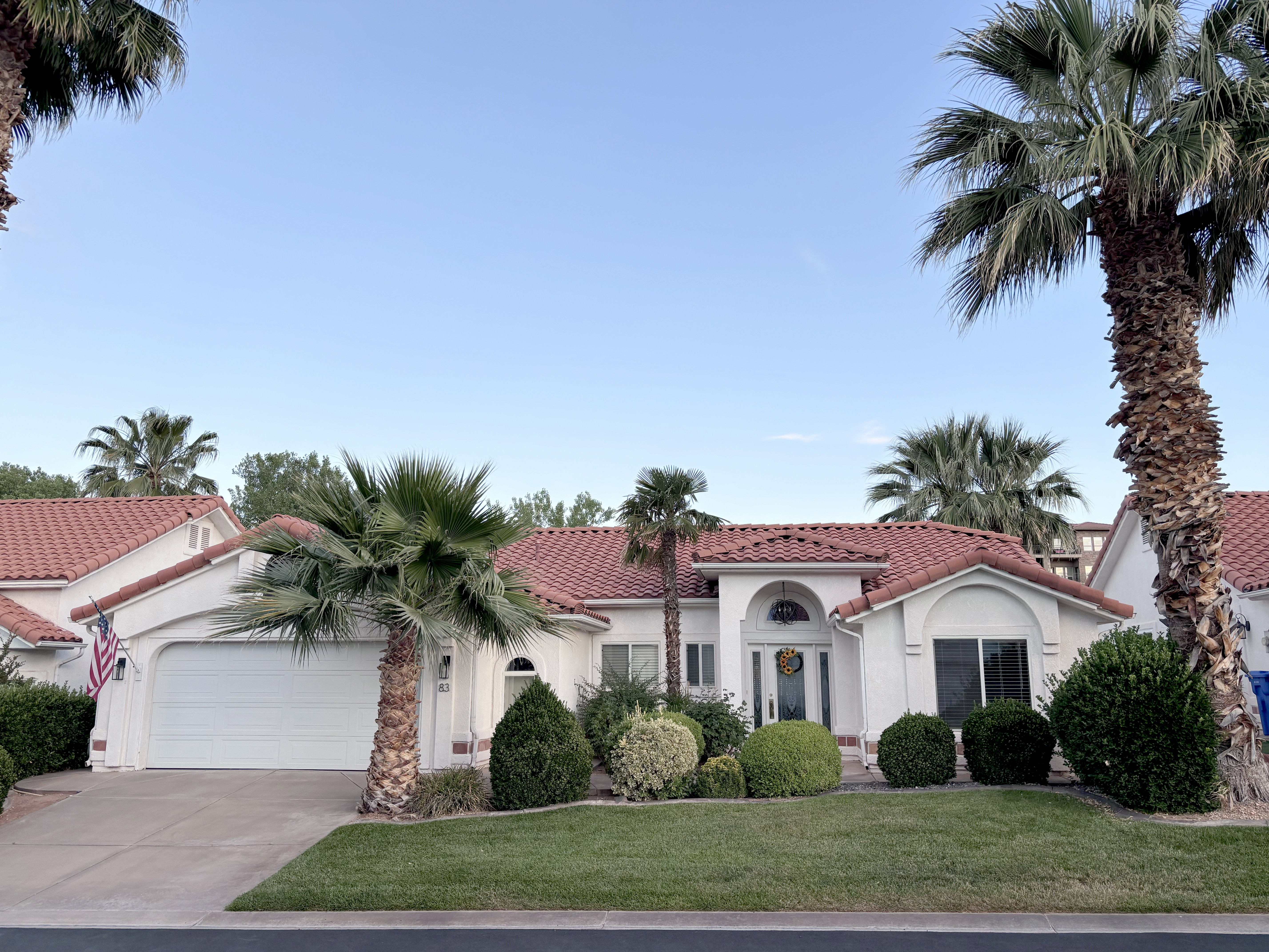 Stucco exterior featuring a red tile roof, arched entry, mature landscaping, an attached garage, and a concrete driveway