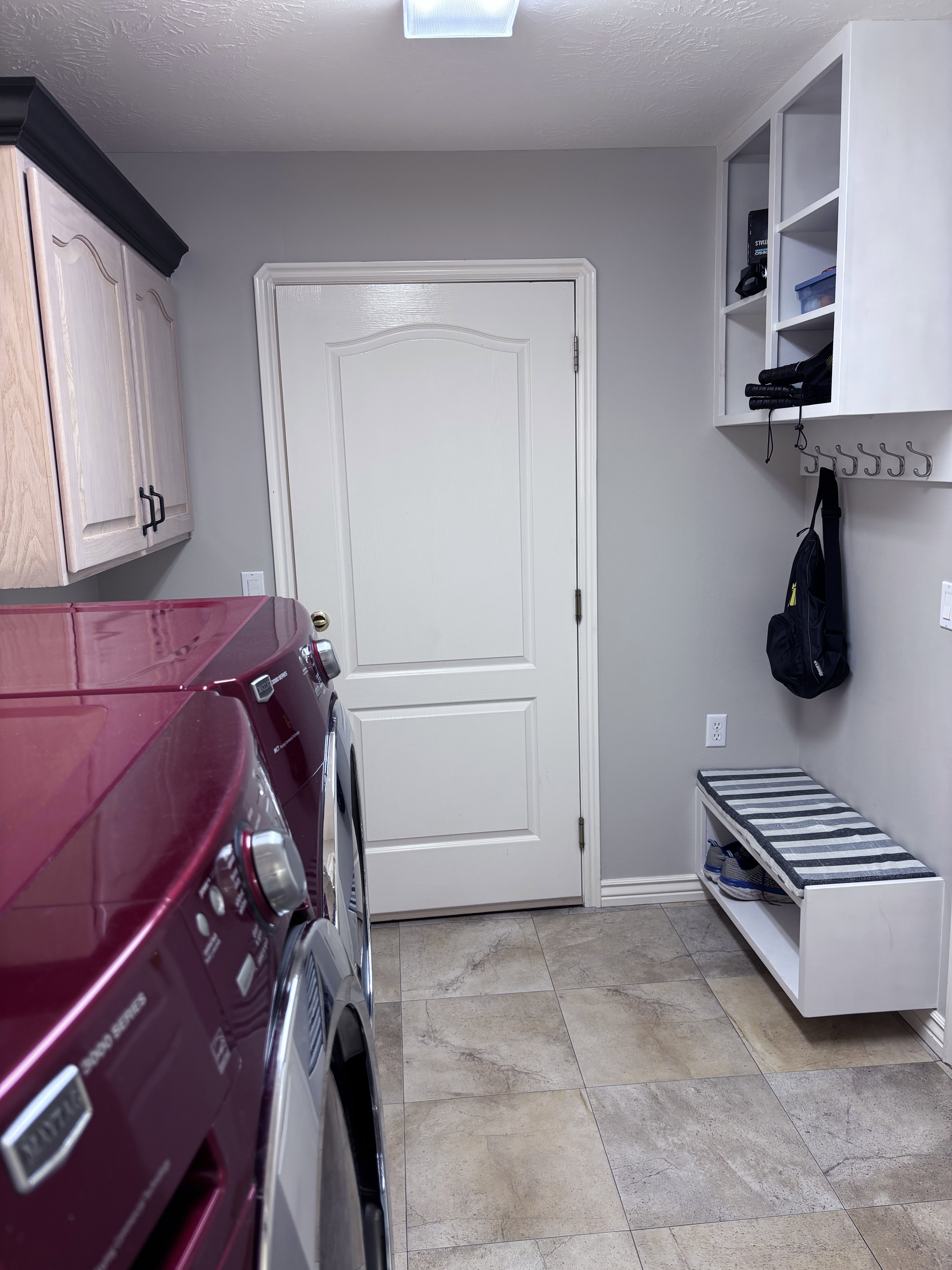 Laundry area featuring wood-finish flooring, light cabinetry with dark hardware, and a built-in storage bench