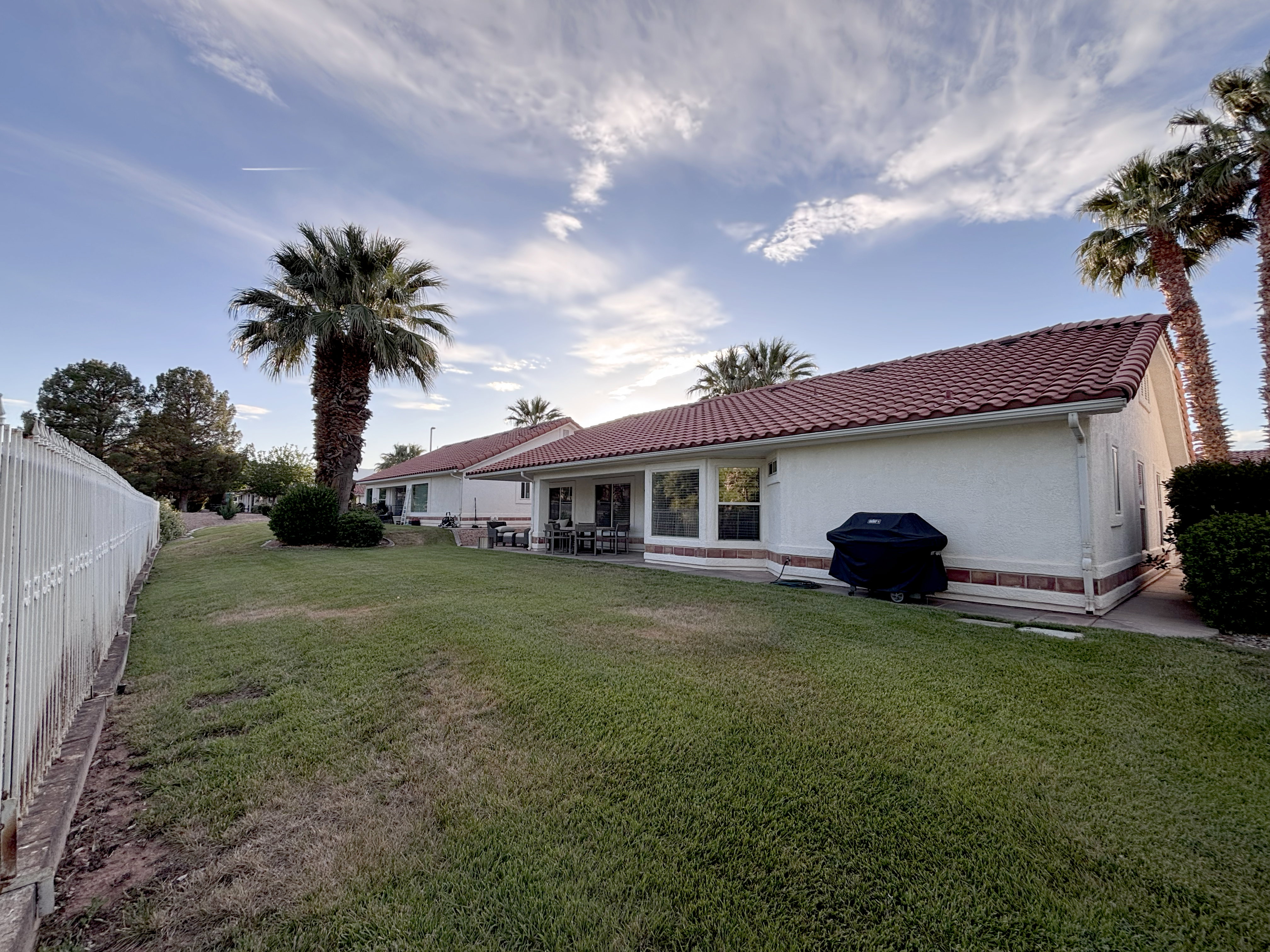 Expansive green lawn with mature palm trees and white fencing