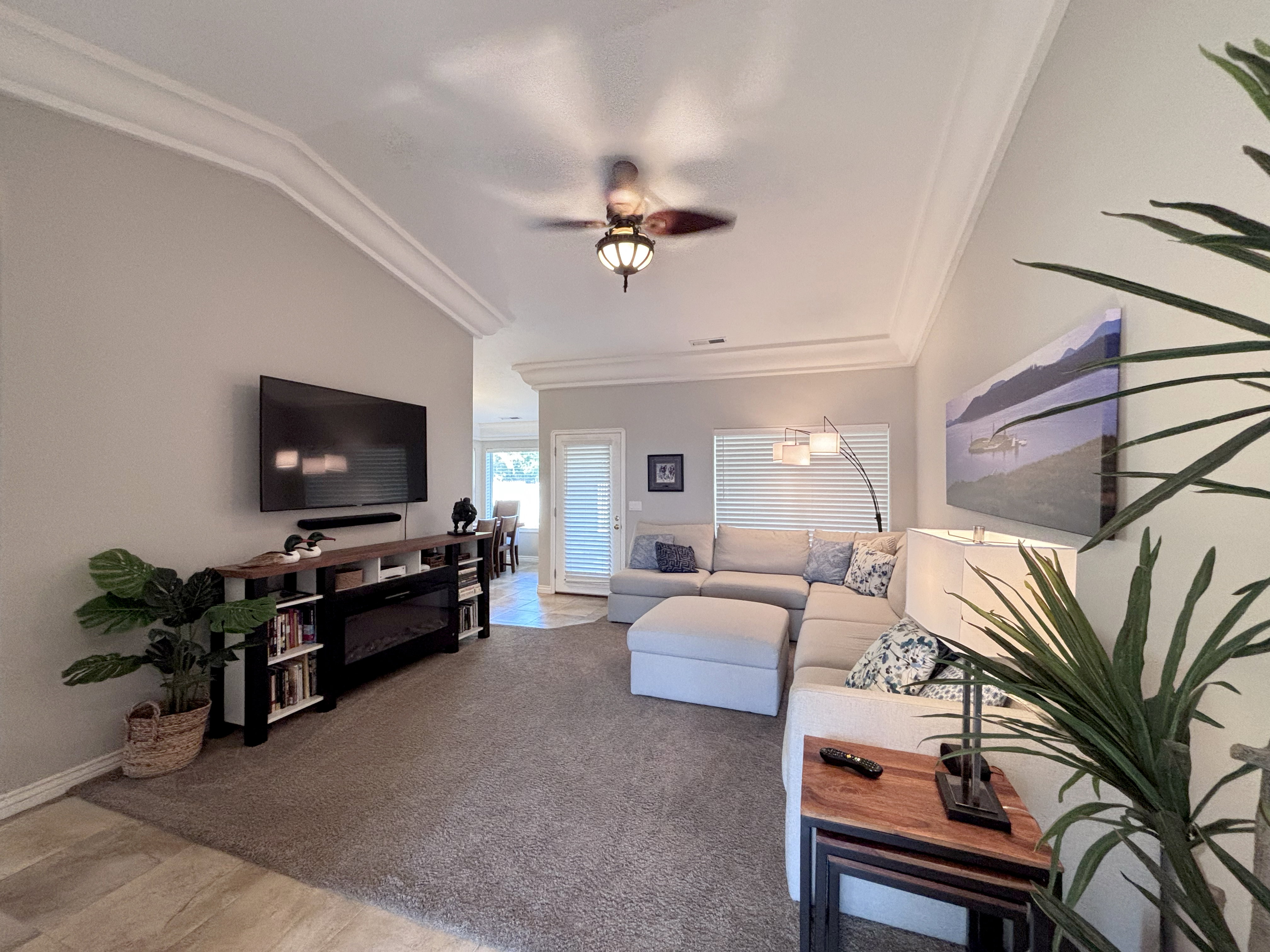 Tray ceiling with crown molding, ceiling fan light fixture, neutral wall paint, and light-filtering blinds