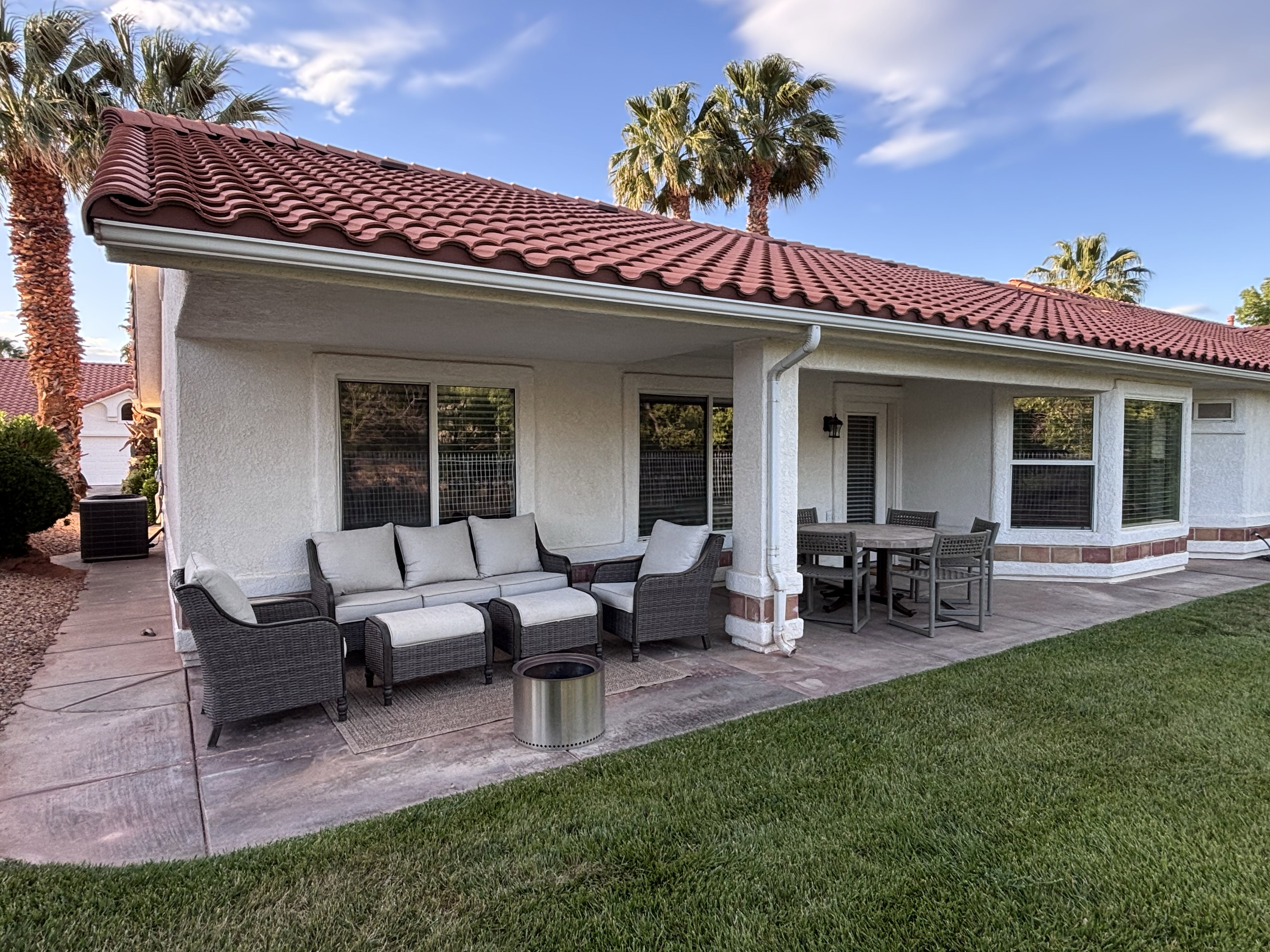 Covered patio with a tile roof, stucco exterior, multiple windows, and a manicured lawn