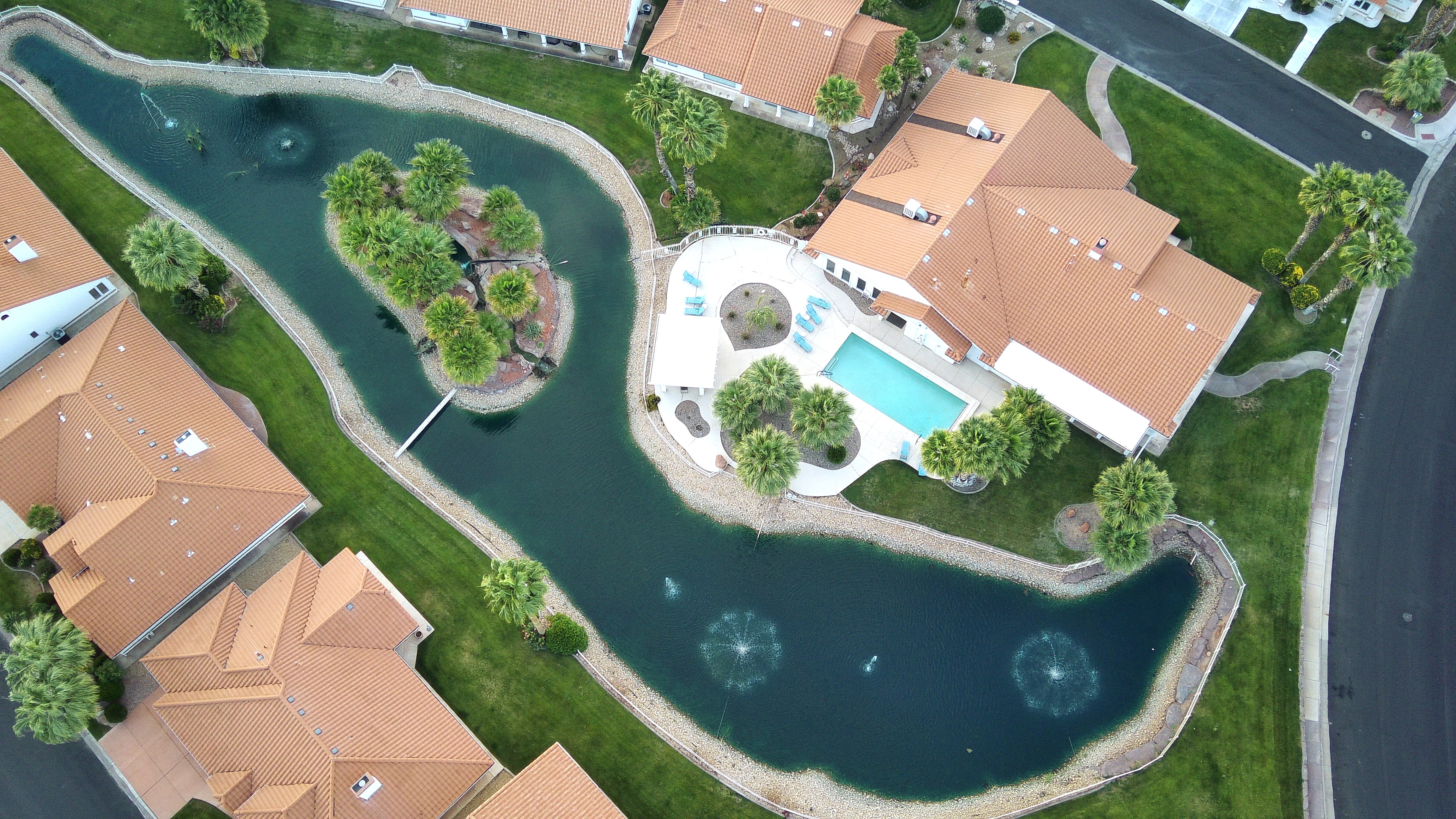 Expansive property featuring a private swimming pool with surrounding patio, a pond with an island, multiple water fountains, and mature palm trees