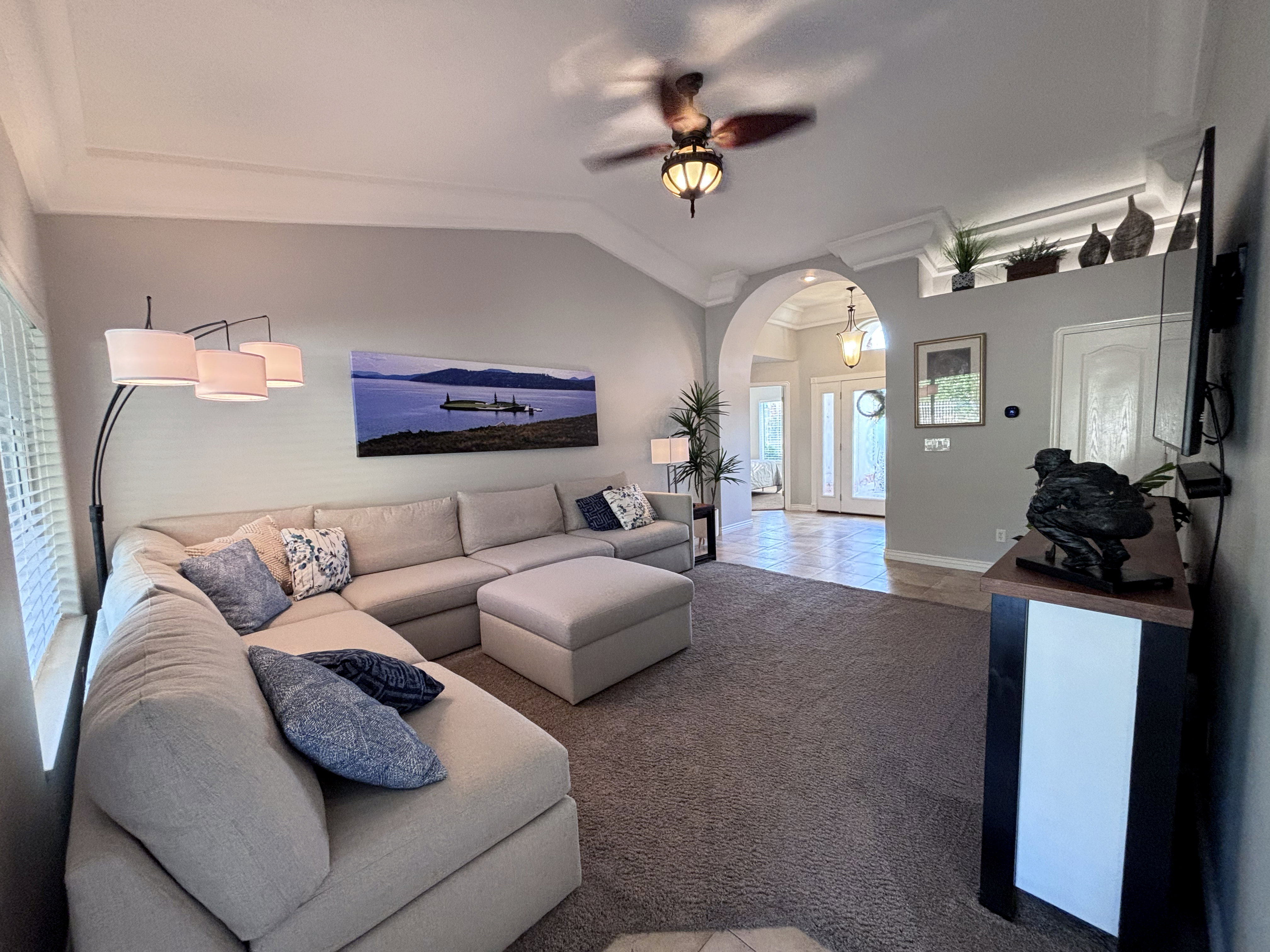 Vaulted ceiling living room featuring crown molding, recessed decorative shelving with accent lighting, and a prominent arched entryway