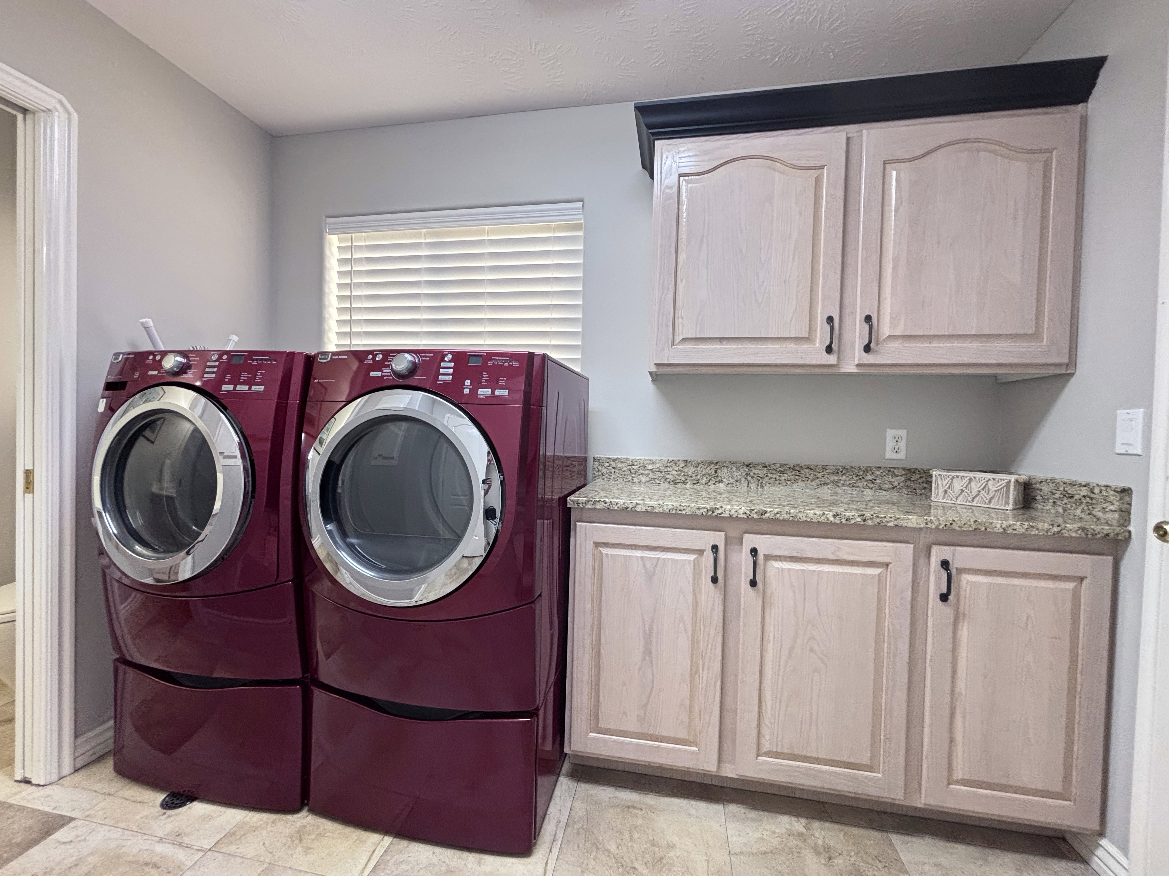 Utility room featuring light wood-finish cabinetry, speckled countertop, and tiled flooring