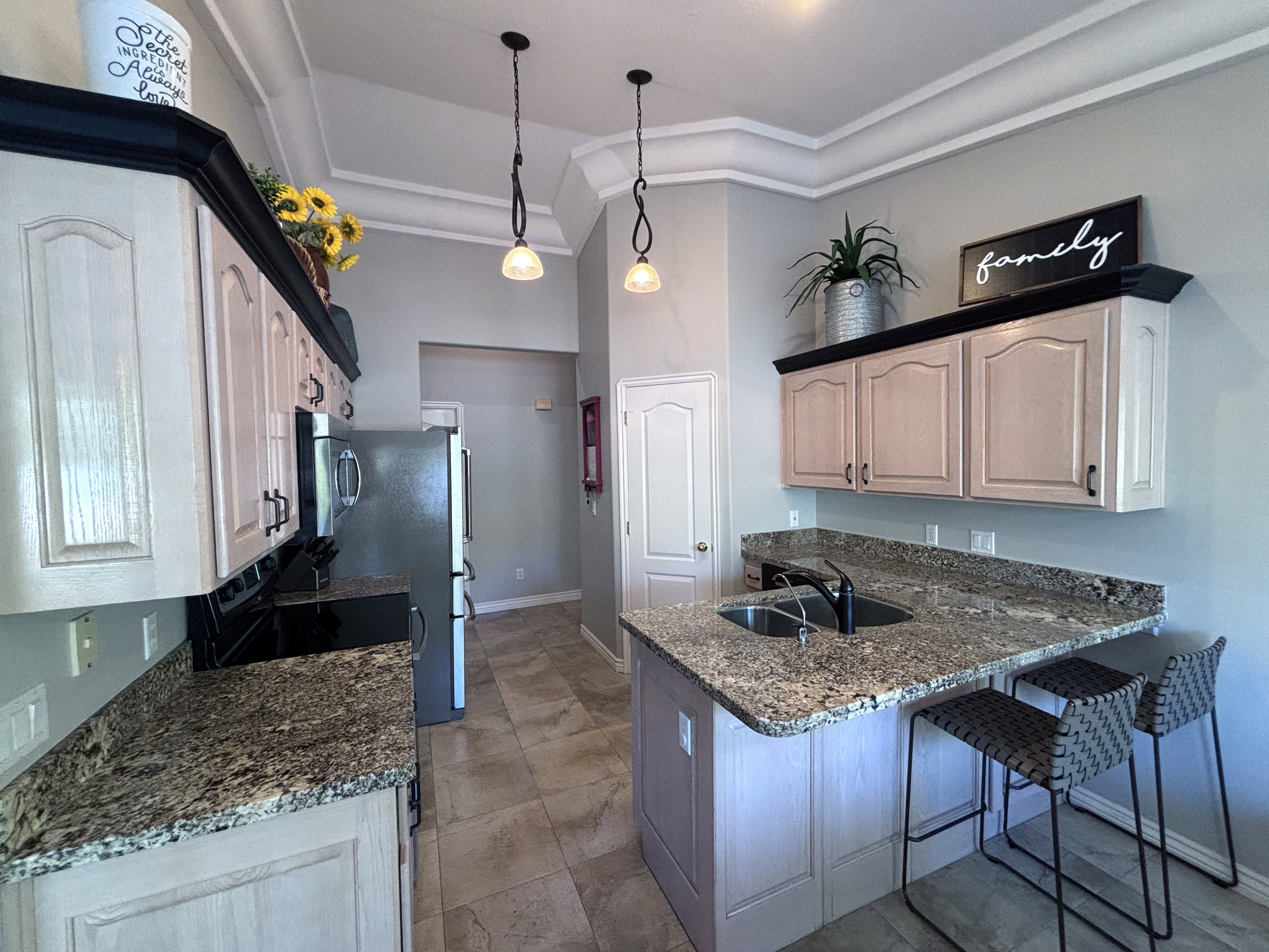 Kitchen featuring granite countertops, light-toned cabinetry with dark accents, stainless steel appliances, a built-in sink, and pendant lighting