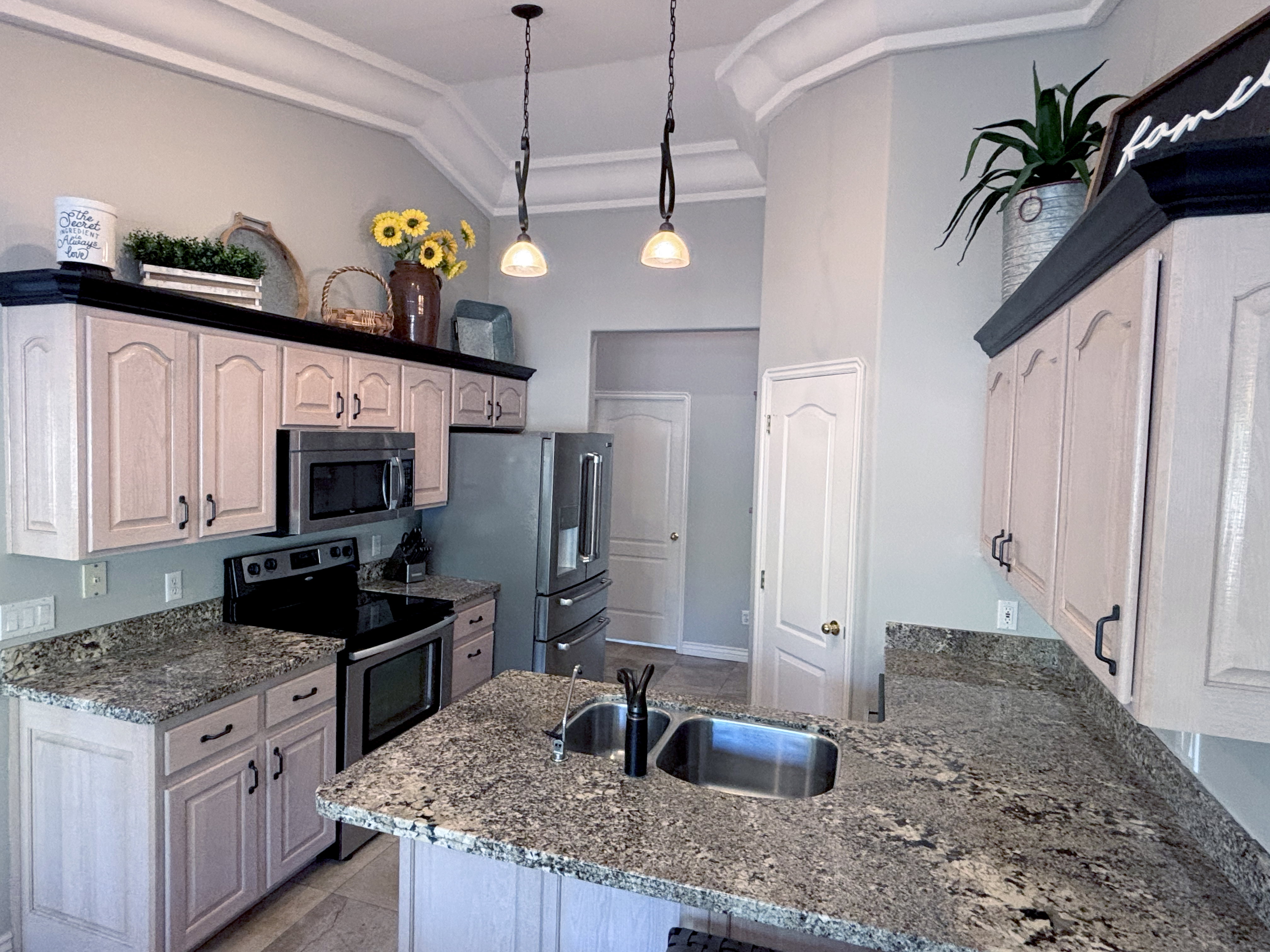 Kitchen featuring a double basin stainless steel sink, light wood-finish cabinetry with dark hardware, stainless steel appliances, and mottled stone countertops