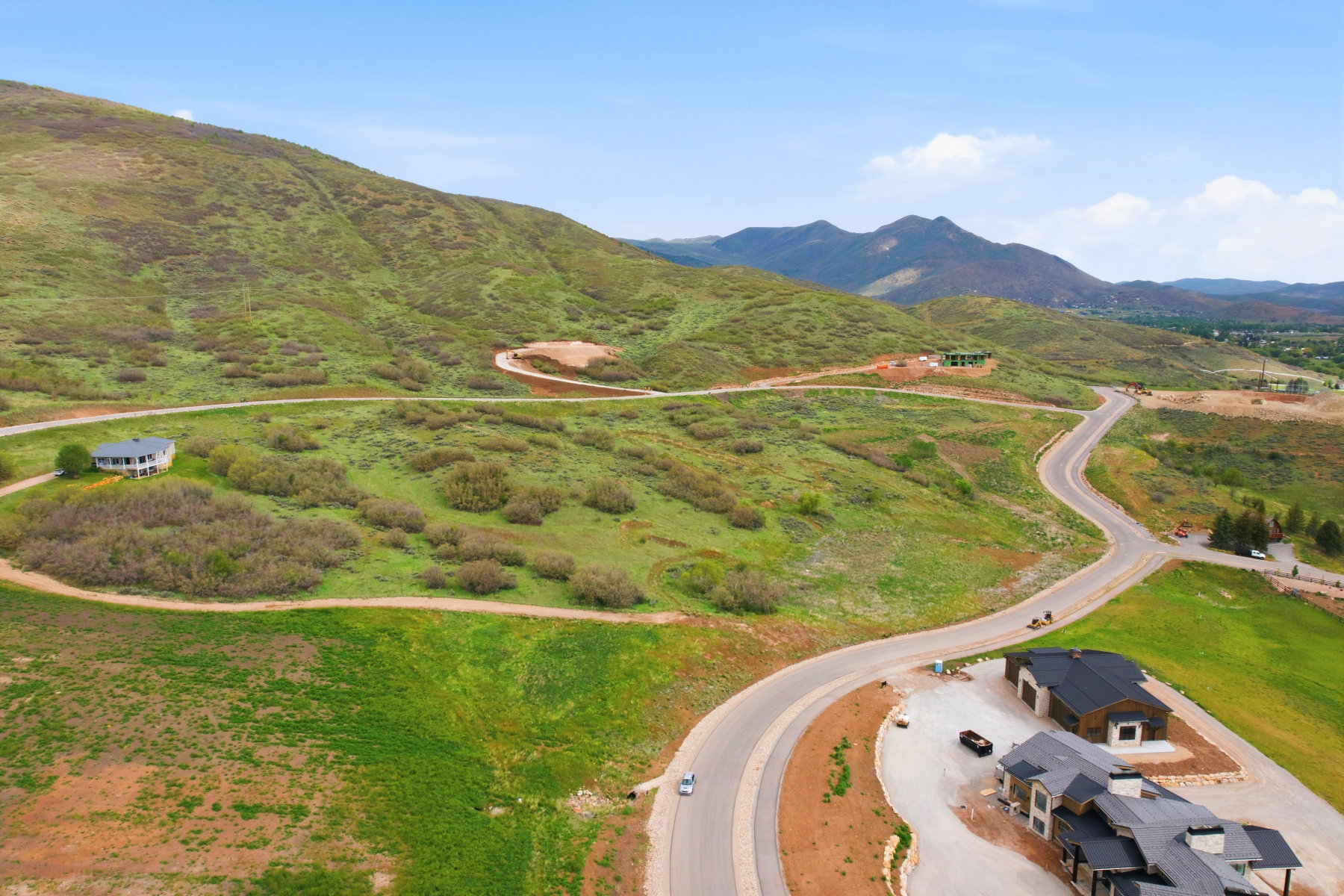 Expansive mountain landscape featuring a paved winding road, multiple building sites, and established properties