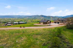 Expansive undeveloped land parcel with a paved road frontage, surrounded by rolling green hills and distant mountain ranges
