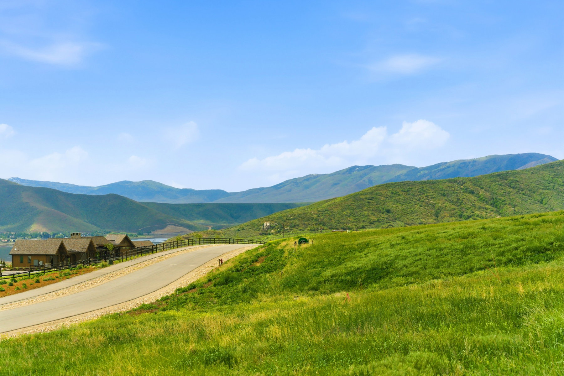 Rolling green hills with a paved road, featuring a distant body of water and mountain range