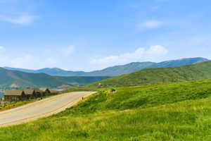 Rolling green hills with a paved road, featuring a distant body of water and mountain range