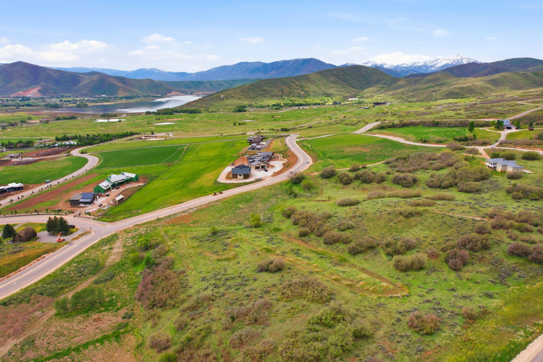 Expansive green landscape with distant mountains featuring snow-capped peaks, a prominent body of water, and residential structures