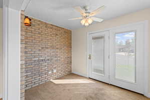 Interior room featuring a prominent brick accent wall, double French doors with integrated blinds, and a ceiling fan with integrated lighting