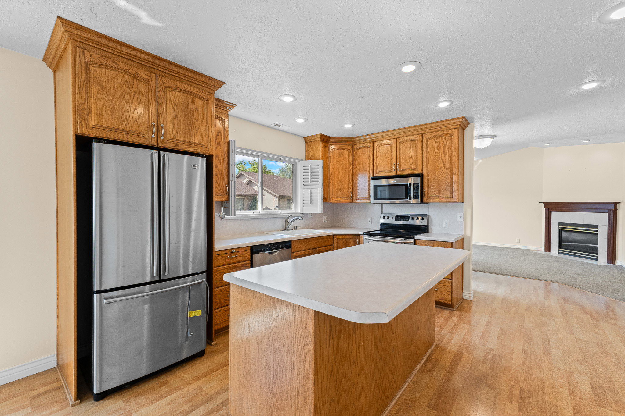 Kitchen featuring wood-finish cabinetry, stainless steel appliances, a center island with a light-toned countertop, recessed lighting, and wood-finish flooring
