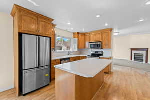 Kitchen featuring wood-finish cabinetry, stainless steel appliances, a center island with a light-toned countertop, recessed lighting, and wood-finish flooring