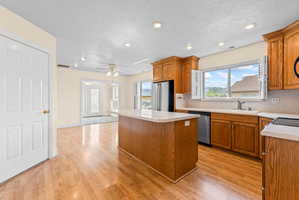 Kitchen featuring wood-finish flooring, wood cabinetry, stainless steel appliances, and a central island with a light-toned countertop