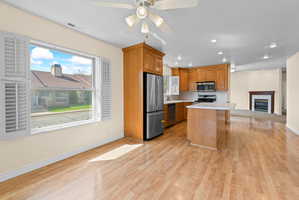 Open-concept living space with wood-finish flooring, a kitchen featuring wood cabinetry and stainless steel appliances, a center island with a white countertop, recessed lighting, and a living area with a fireplace