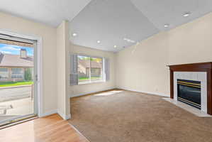 Living area featuring a fireplace with a wood-finish mantel and tile surround, recessed lighting, vaulted ceiling, and a large window with white louvered shutters