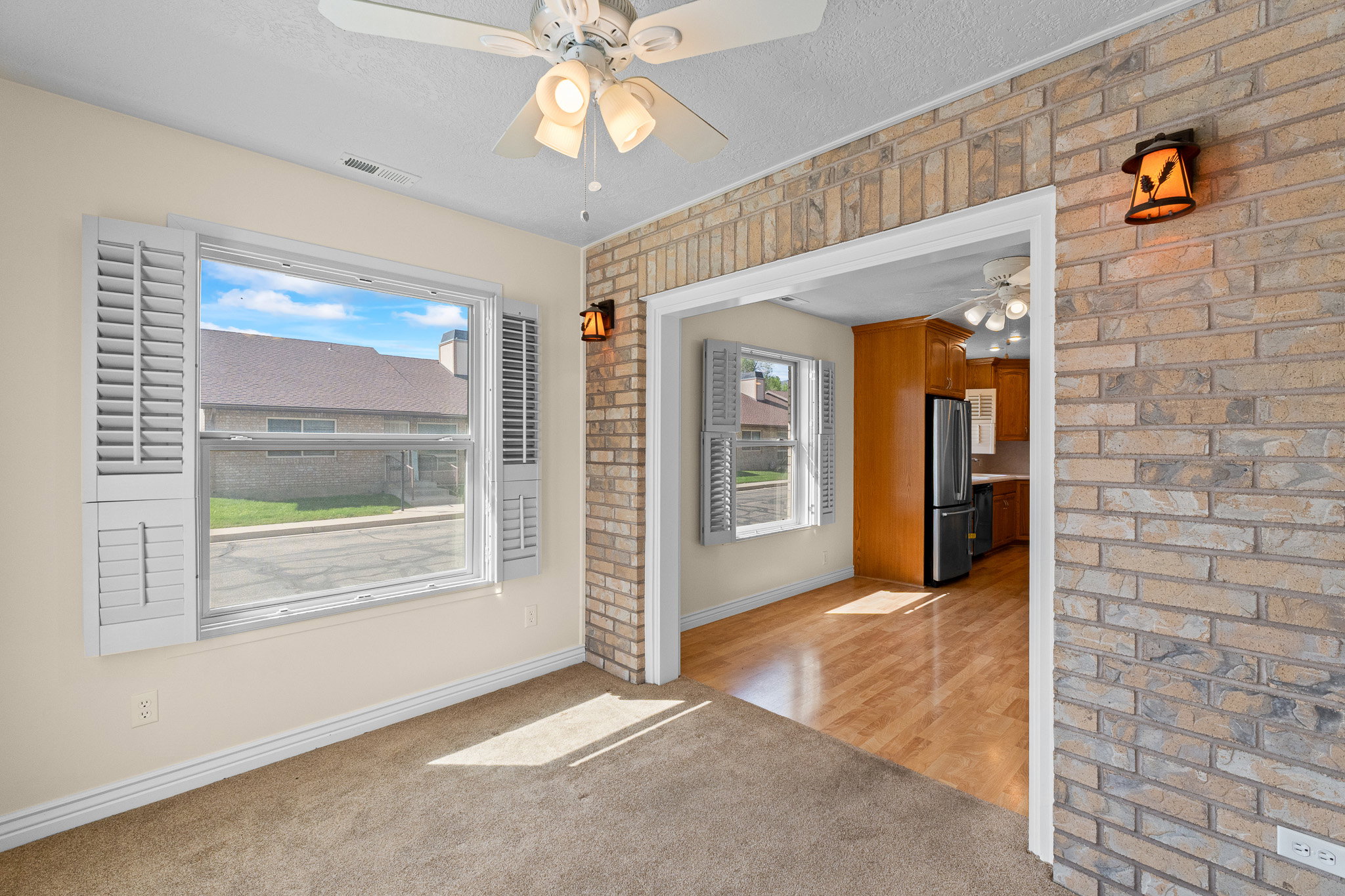 Interior room featuring neutral wall paint, carpet flooring, a ceiling fan with integrated lighting, and a large window with white louvered shutters