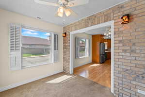Interior room featuring neutral wall paint, carpet flooring, a ceiling fan with integrated lighting, and a large window with white louvered shutters