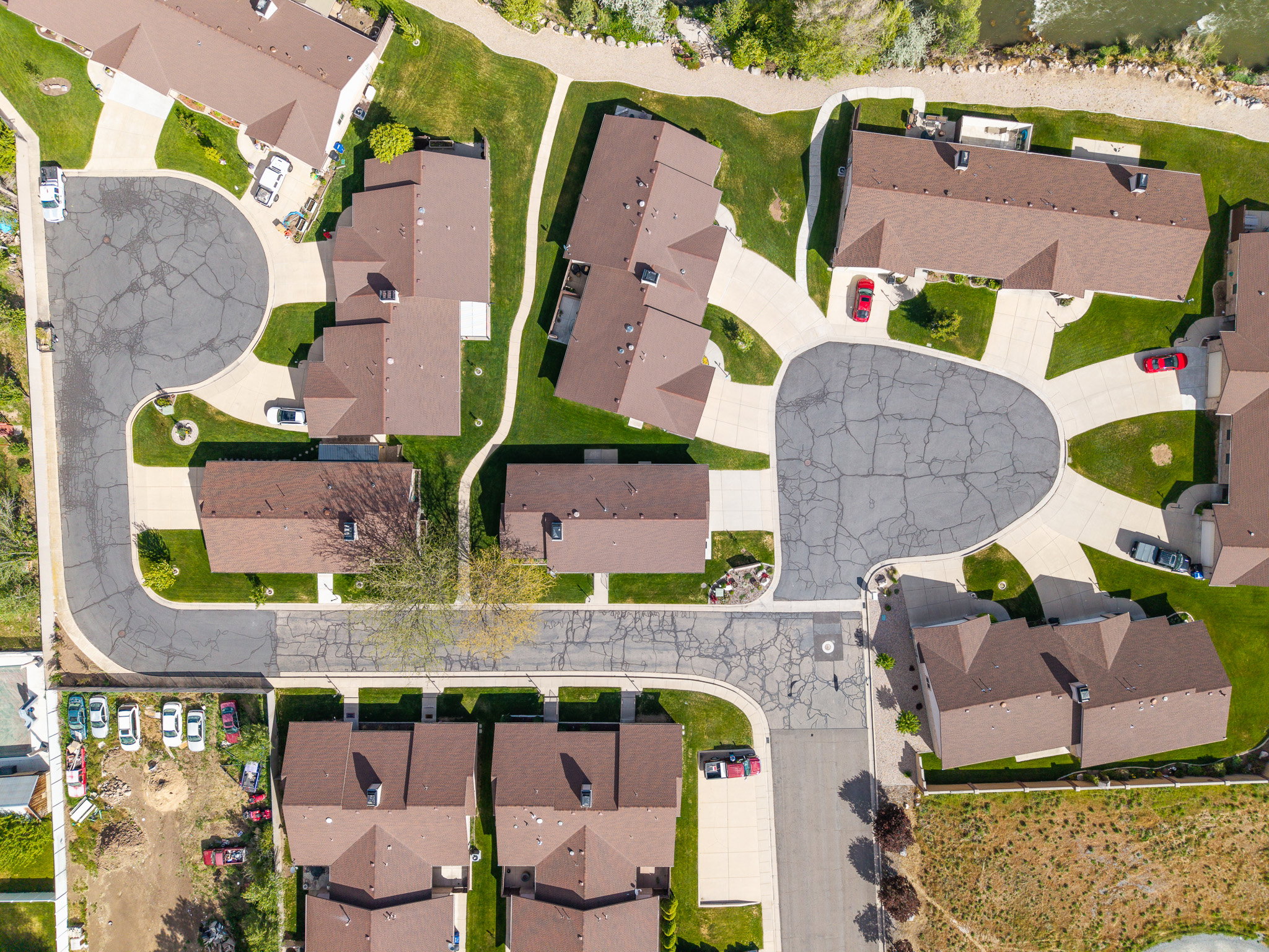 Aerial view of a residential community featuring multiple brown-roofed structures, paved driveways, and manicured green spaces