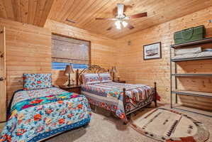 Room featuring natural wood-paneled walls and ceiling, a window with a woven shade, and neutral carpet flooring