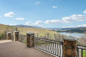 Spacious outdoor patio featuring stone-clad pillars, wrought iron railings, and a vast natural landscape with distant water