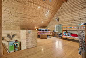 Spacious loft area featuring wood-finish flooring, vaulted wood-plank ceilings, recessed lighting, and log-style wall finishes
