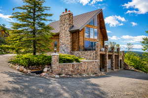 Log cabin exterior featuring a prominent stone chimney and a full-height window wall