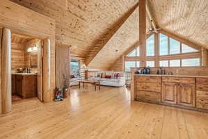 Expansive wood-paneled interior featuring vaulted ceilings with exposed beams, wood-finish flooring, and a stone-look countertop on a built-in wood cabinet