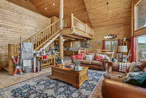 Spacious open-concept living area featuring a vaulted wood-plank ceiling, natural wood walls, and a prominent wood staircase leading to an upper-level balcony
