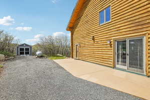Log cabin exterior featuring a paved patio, dual sliding glass doors, upper-level window, and exterior lighting fixtures