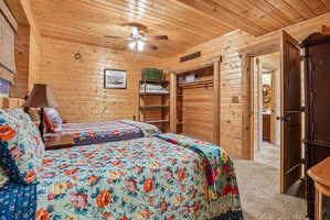 Interior room featuring wood-paneled walls and ceiling, a ceiling fan, plush carpet flooring, a built-in closet with shelving, and a wood-finish door leading to an additional space