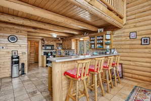 Log cabin interior featuring a kitchen with light wood cabinetry, a breakfast bar with a light-colored countertop, and tiled flooring