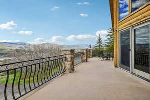 Expansive outdoor terrace featuring stone pillars, decorative wrought iron railing, and a log-style exterior with large glass sliding doors
