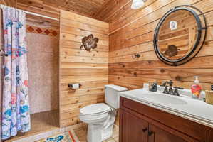 Bathroom featuring wood-paneled walls and ceiling, a walk-in shower with tile surround, a single vanity with a white countertop and dark wood-finish cabinetry, and a round wall-mounted mirror