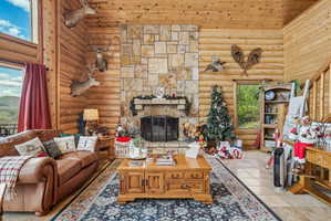 Expansive living area featuring log walls, a stone-clad fireplace with a hearth, tile flooring, and a large window providing ample natural light