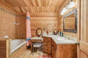 Bathroom featuring extensive wood paneling on walls and ceiling, a built-in vanity with light-colored countertop, and an integrated sink with brass-finish faucet
