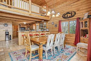 Open-concept dining area featuring natural wood log walls, a wood-finish vaulted ceiling, and tile flooring