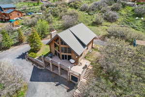 Rustic wood-sided home featuring a prominent A-frame window wall, a stone chimney, a multi-level deck, a stone retaining wall, and a multi-pitched roofline