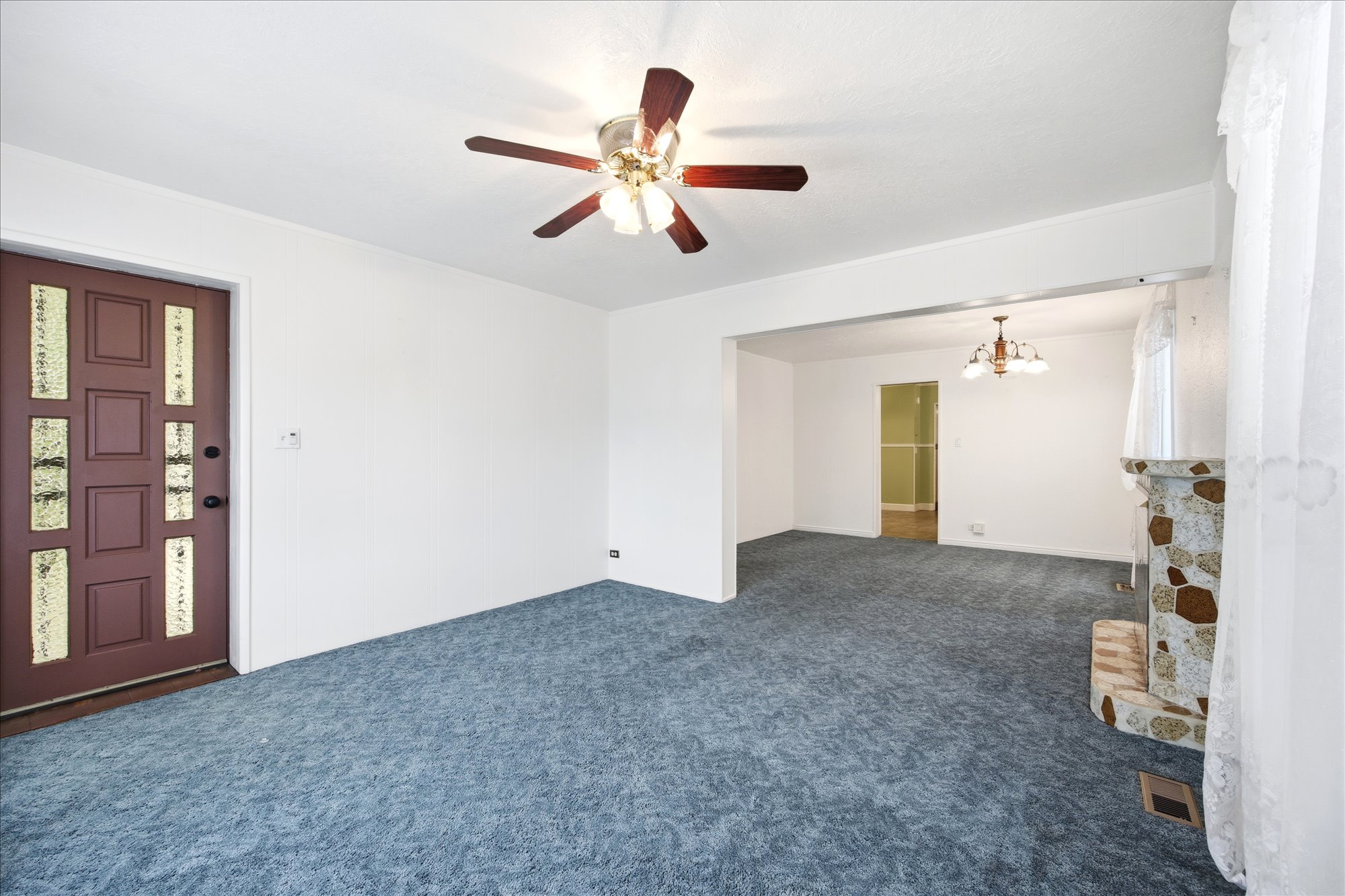 Spacious interior featuring a decorative entry door, ceiling fan with integrated lighting, and a stone-clad fireplace