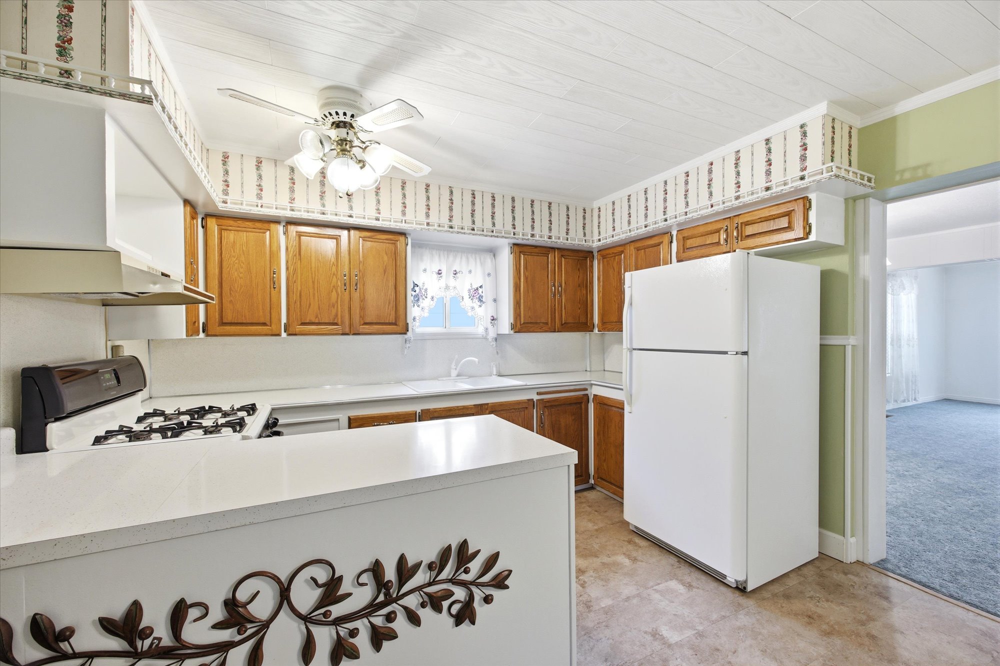 Kitchen featuring wood-finish cabinetry, white countertops, a gas range with an overhead vent, and a ceiling fan with integrated lighting