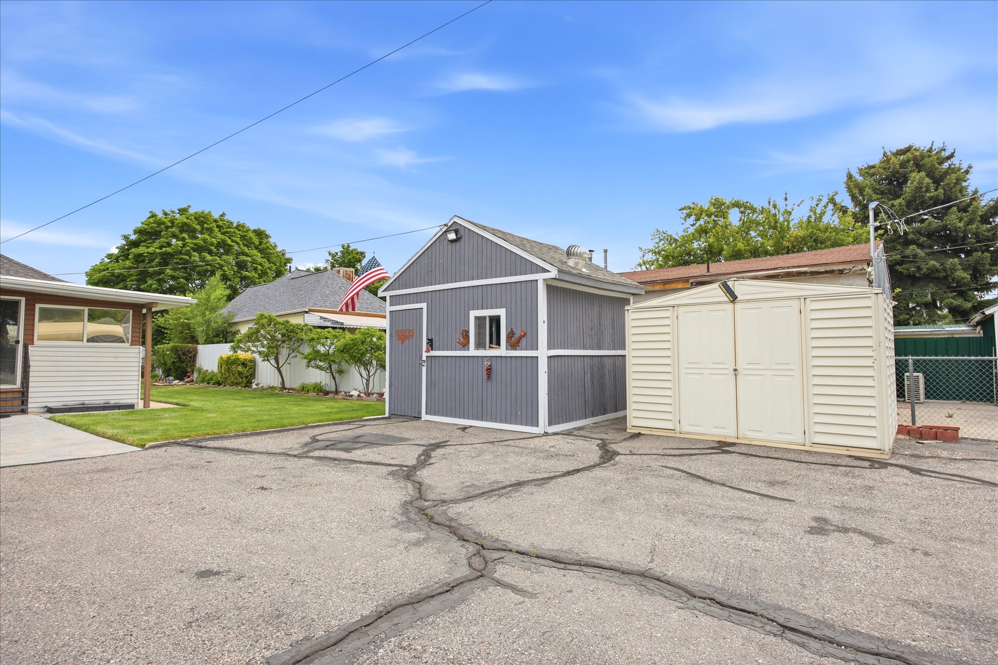 Expansive paved area featuring a grey utility building with a single window and an adjacent cream-colored storage shed