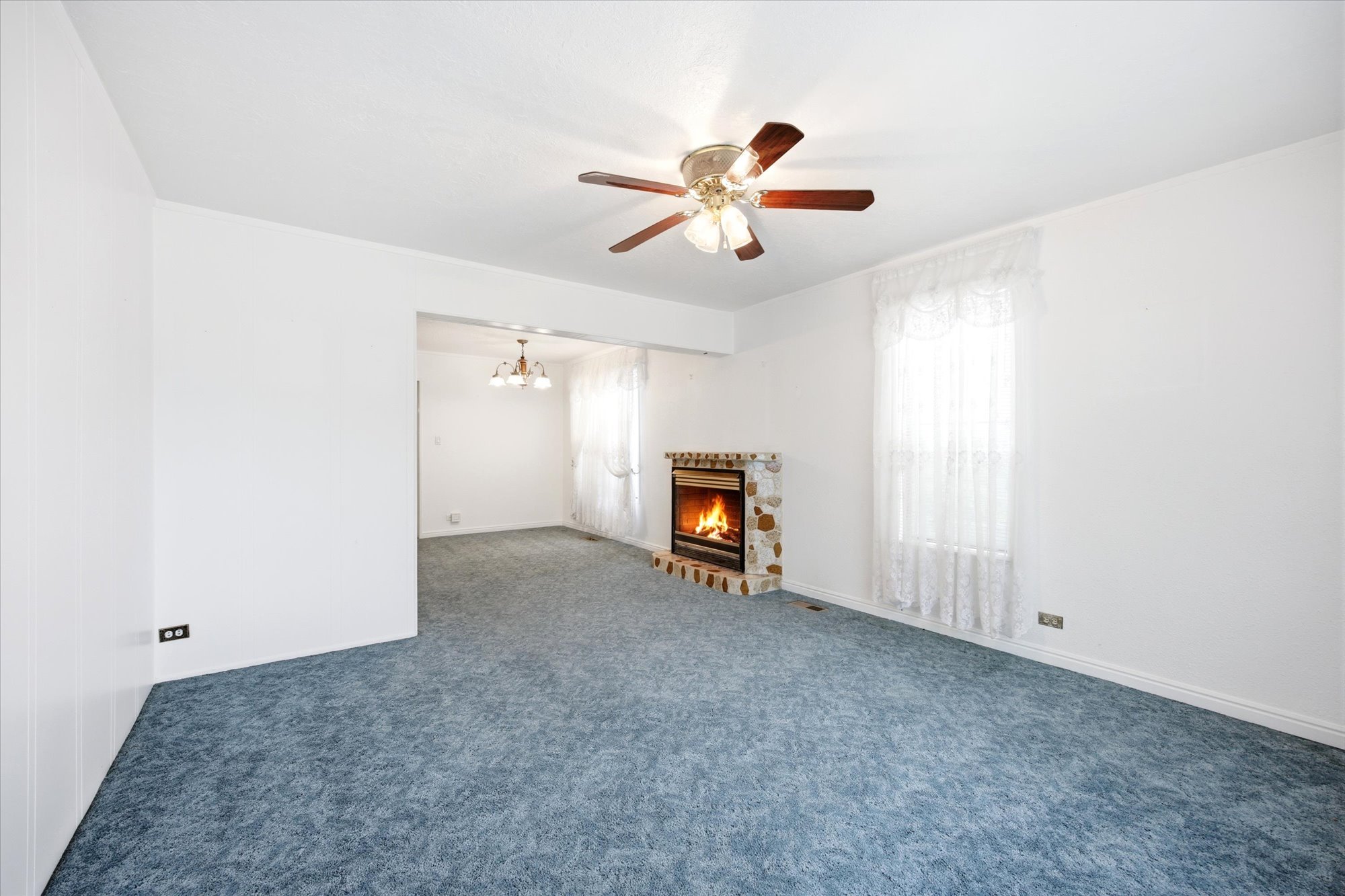 Living area featuring a stone fireplace, ceiling fan with wood-finish blades, and blue carpet