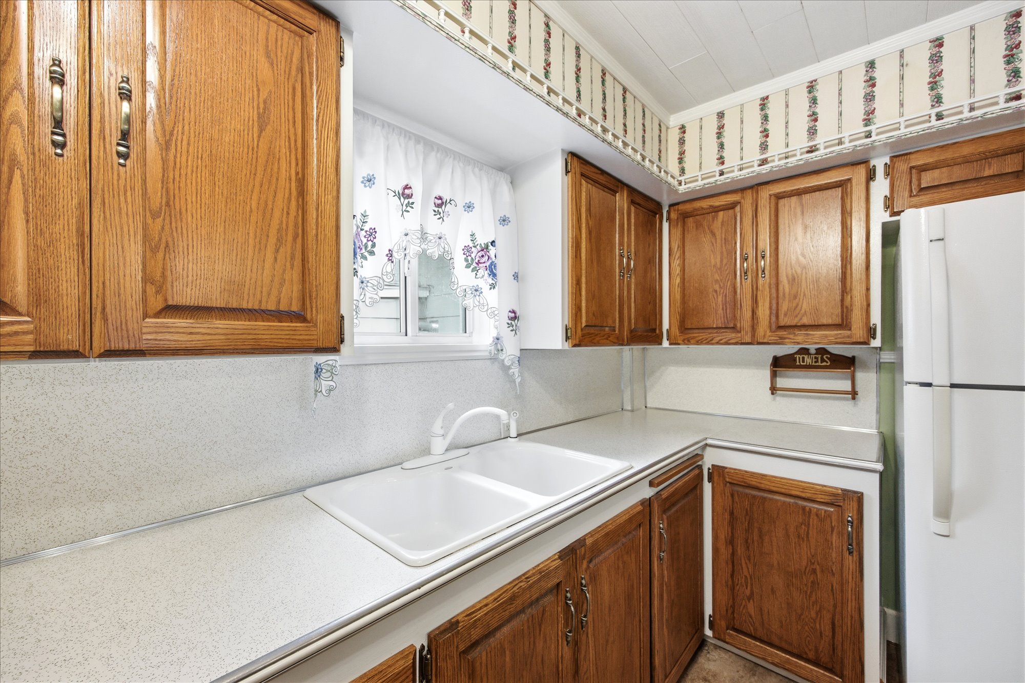 Kitchen featuring a white double basin sink, white countertops, wood-finish cabinetry, and a white refrigerator