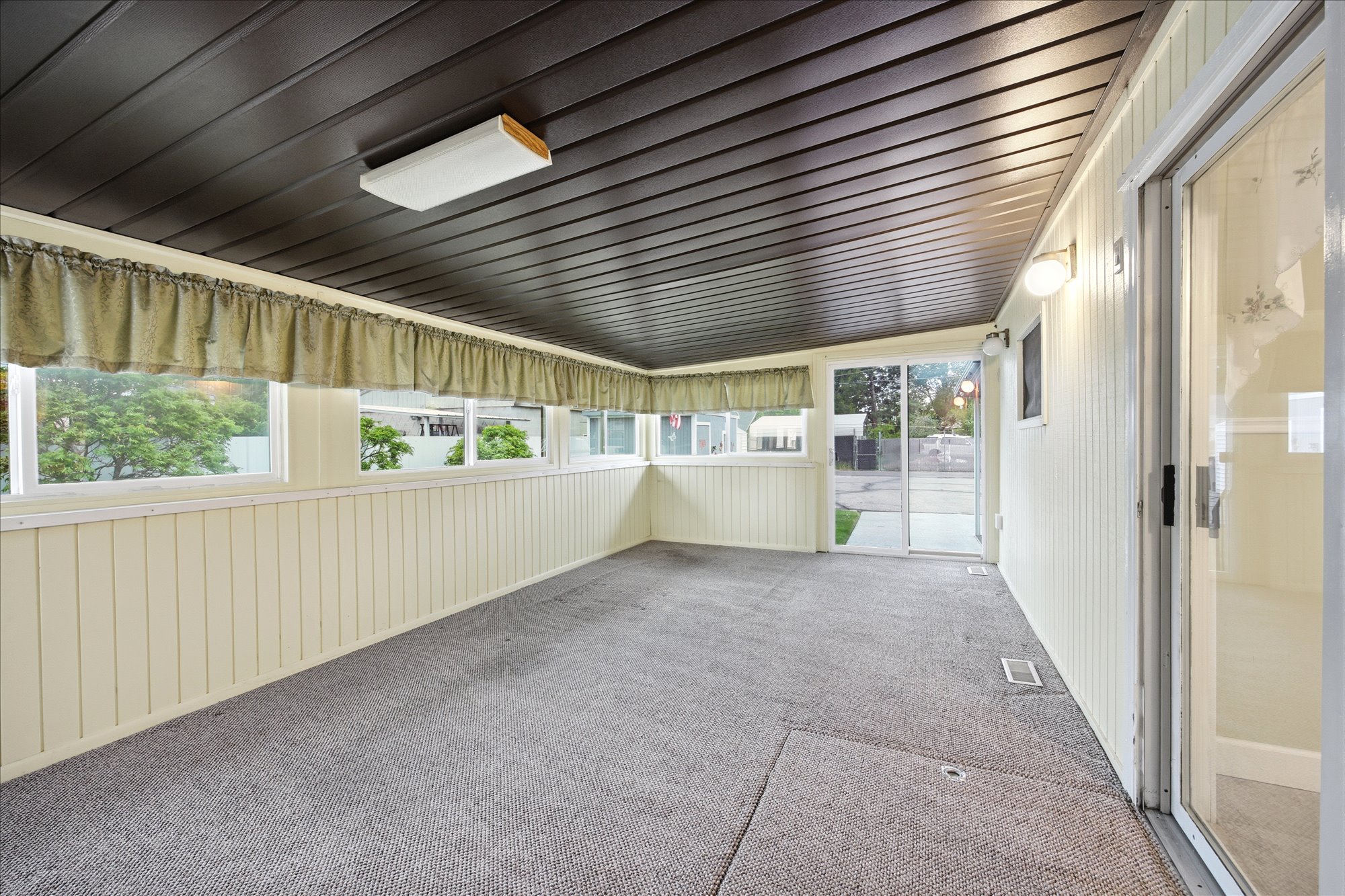 Enclosed patio featuring durable carpeting, board and batten wall paneling, and a dark wood-finish plank ceiling