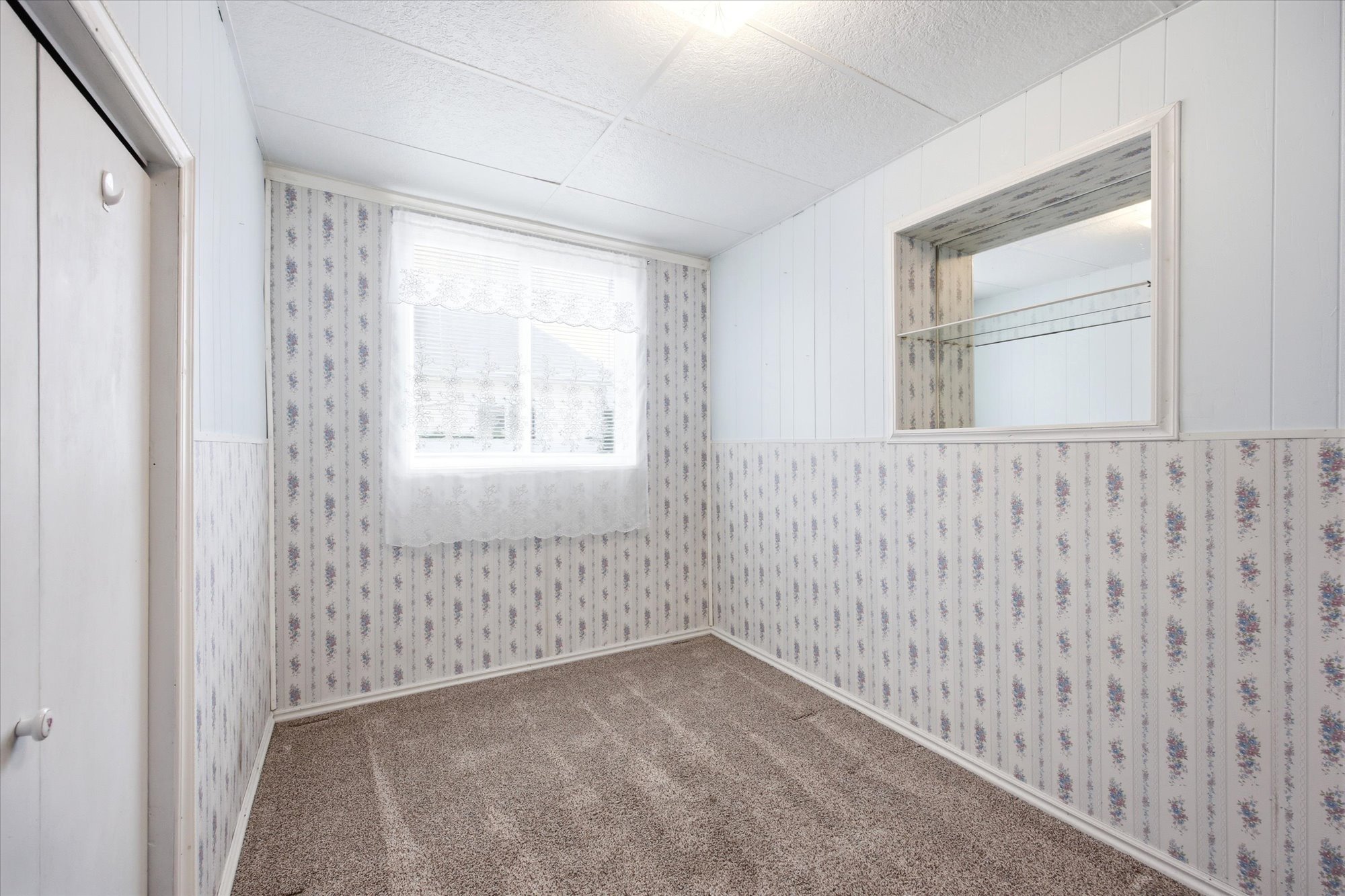 Room featuring textured carpet flooring and patterned wallpaper with a white chair rail
