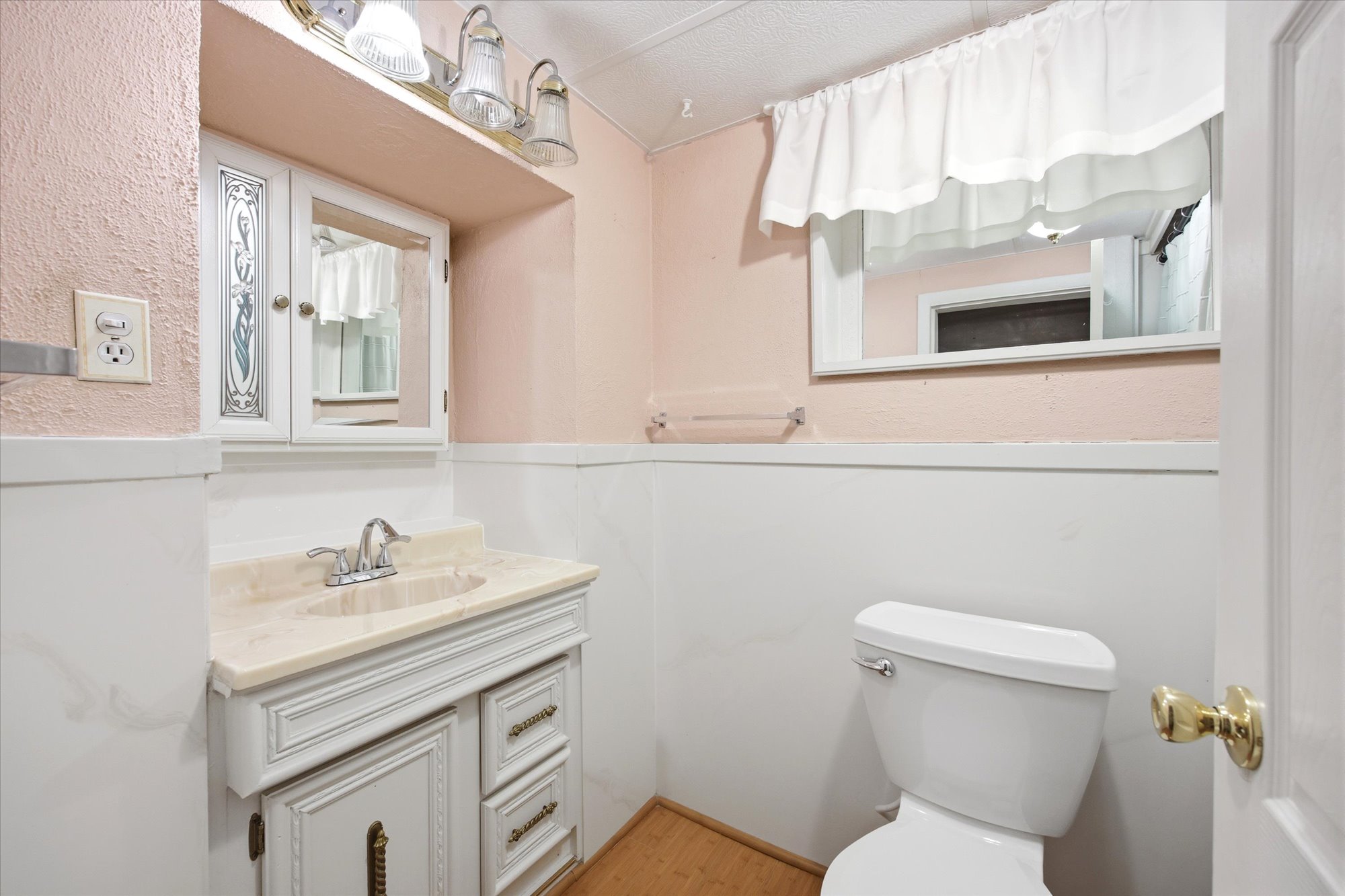 Bathroom featuring a single vanity with a built-in sink, wall-mounted medicine cabinet, toilet, and a window with a valance