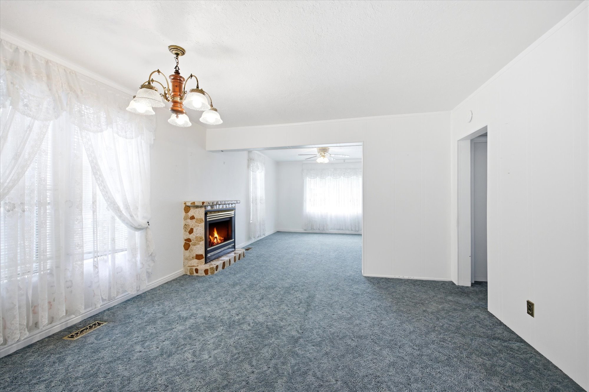Living area featuring a stone fireplace with a metal insert, white walls, and blue carpet