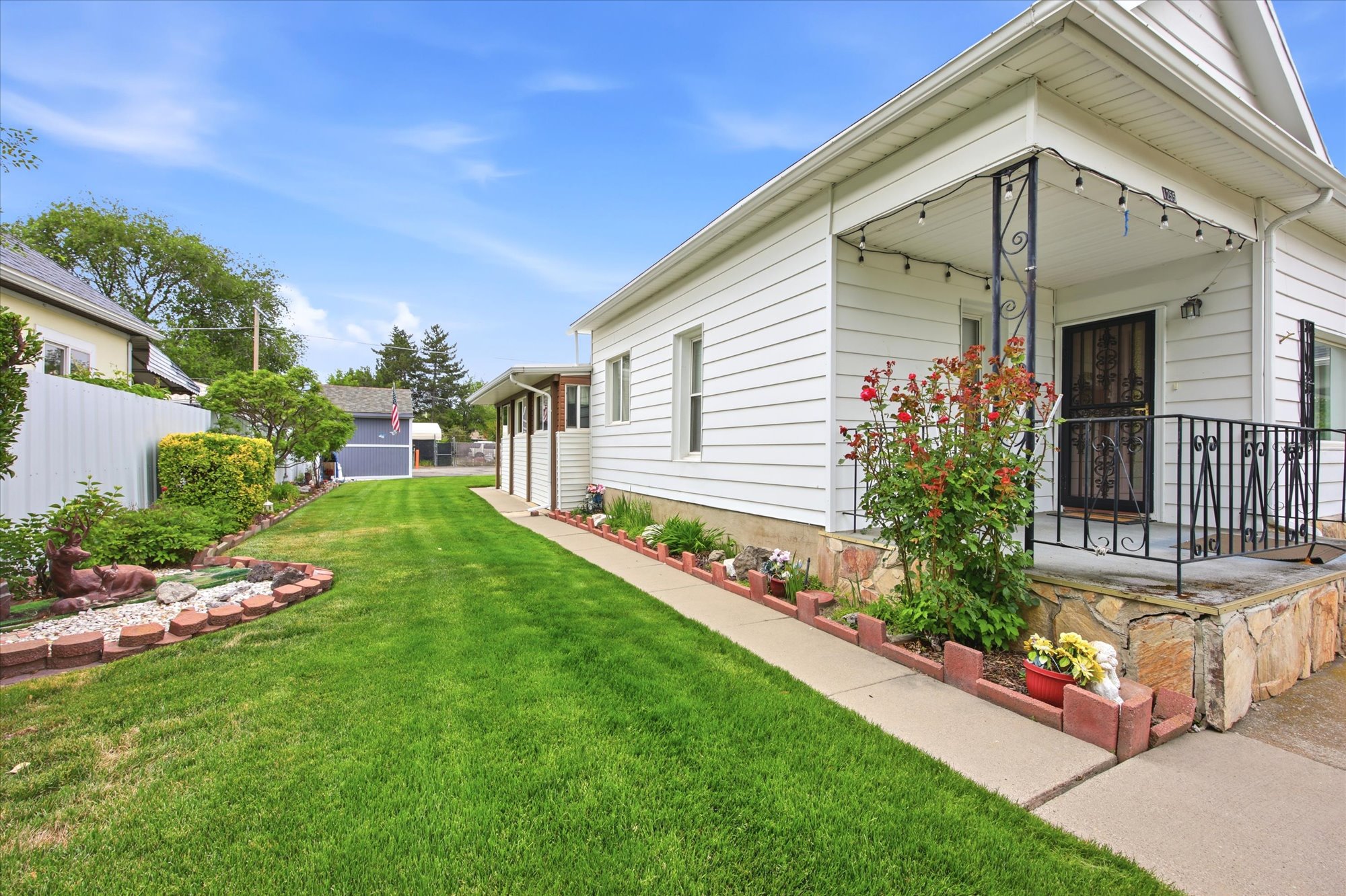 Exterior featuring white siding, a covered porch with black wrought iron railing, and a concrete walkway