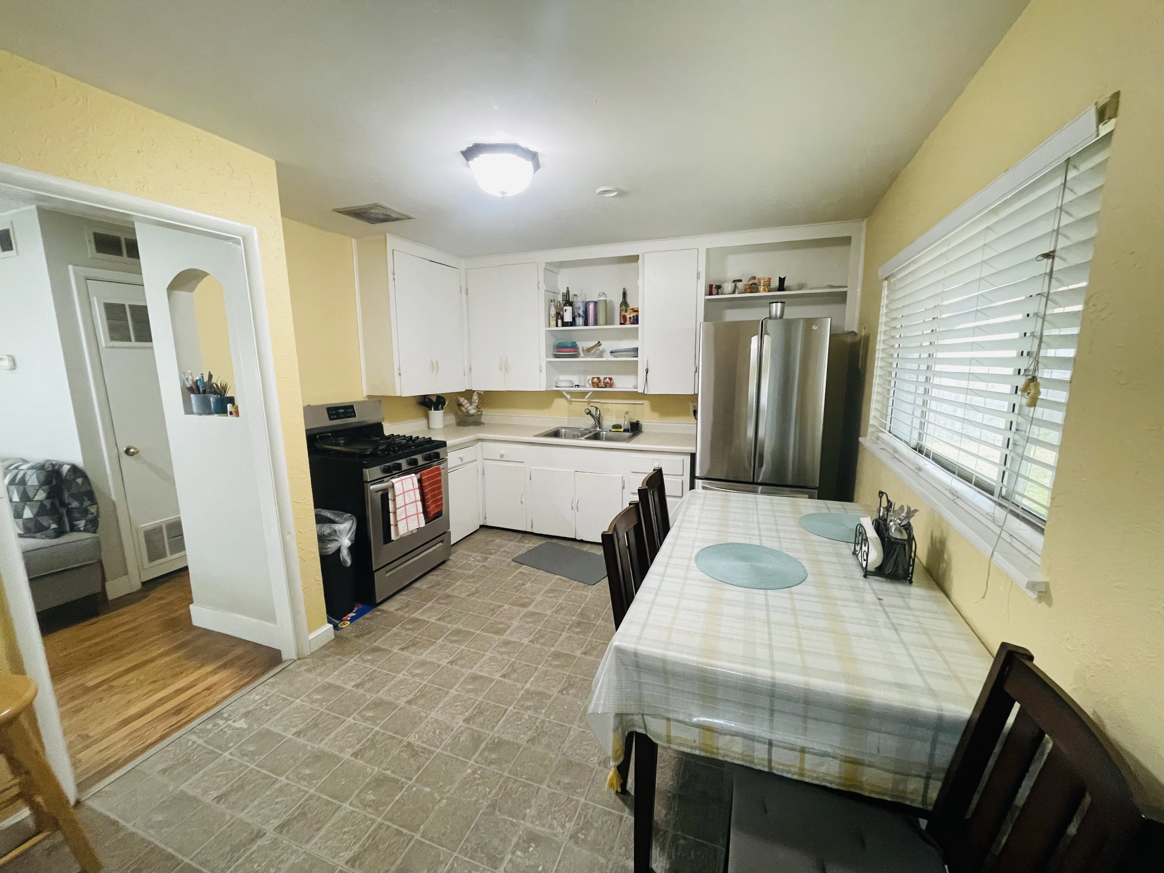 Kitchen featuring white cabinetry, stainless steel appliances including a gas range and refrigerator, and a window with blinds